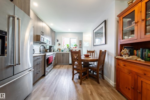 Galley kitchen featuring wood-finish flooring, stainless steel appliances, light wood-grain cabinetry, recessed lighting, and a white subway tile backsplash - 10811 73 Avenue, Edmonton, AB 