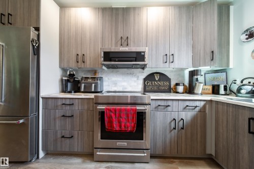 Contemporary kitchen featuring wood-finish cabinetry with black hardware, stainless steel appliances, and a tiled backsplash - 10811 73 Avenue, Edmonton, AB 