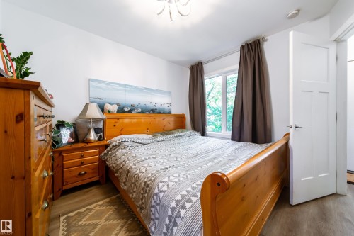 Bedroom featuring light wood-finish flooring, a white paneled door with contemporary hardware, and a window with dark drapery - 10811 73 Avenue, Edmonton, AB 