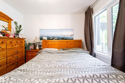 Bright bedroom featuring a large window with white trim, wood-finish flooring, and white walls - 10811 73 Avenue, Edmonton, AB 