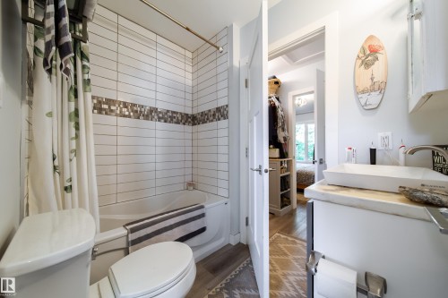 Bathroom featuring a white subway tile surround with mosaic accent, a soaking tub, and a white toilet - 10811 73 Avenue, Edmonton, AB 