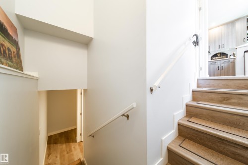 Interior staircase featuring wood-finish treads with safety strips, white risers, and a white wall-mounted handrail - 10811 73 Avenue, Edmonton, AB 