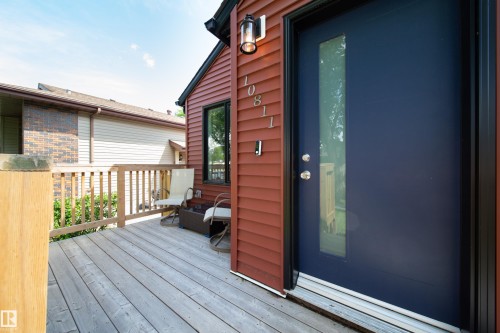 Inviting front entry featuring a rich red siding, a contemporary navy blue door with a vertical glass insert, and a spacious wood-finish deck - 10811 73 Avenue, Edmonton, AB 