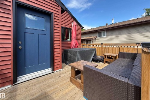 Expansive wood decking featuring a red horizontal siding exterior with a blue entry door, privacy fencing, and a small window - 10811 73 Avenue, Edmonton, AB 