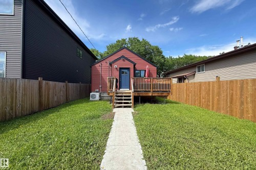 Rear exterior featuring red siding, a raised wood deck, and a blue entry door - 10811 73 Avenue, Edmonton, AB 