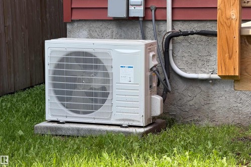 Exterior mini-split HVAC unit mounted on a concrete pad, against a stucco foundation with red siding - 10811 73 Avenue, Edmonton, AB 
