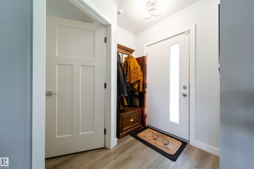Entryway featuring wood-finish flooring, a white paneled interior door with a brushed nickel lever, and a white front door with a vertical glass insert - 10811 73 Avenue, Edmonton, AB 