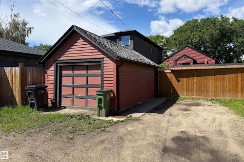 Detached garage with horizontal red siding, a black-framed garage door, and a dark shingled roof - 10811 73 Avenue, Edmonton, AB 