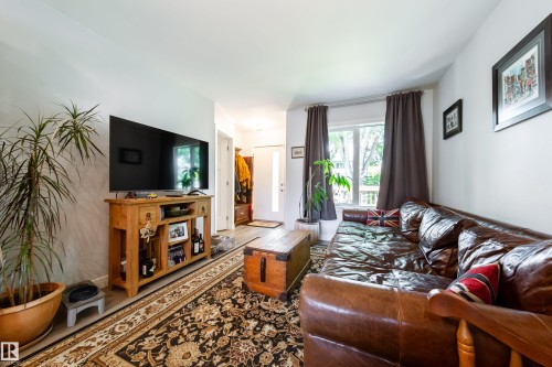 Bright living area featuring light-toned walls, wood-finish flooring, and a large window with privacy drapes - 10811 73 Avenue, Edmonton, AB 