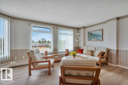 Living area featuring multiple windows with vertical blinds, wood-finish flooring, and a drop ceiling - 316 2011 137 Avenue, Edmonton, AB - Indoor Photo Showing Living Room