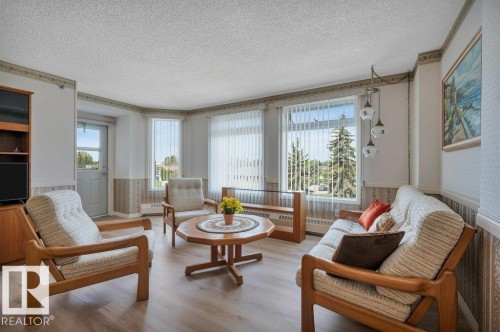 Living area featuring wood-finish flooring, multiple windows with vertical blinds, a visible exterior door, and a multi-pendant ceiling light fixture - 316 2011 137 Avenue, Edmonton, AB - Indoor Photo Showing Living Room