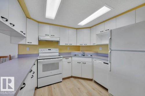Kitchen featuring extensive white cabinetry, light wood-finish flooring, a double basin sink, and integrated white appliances - 316 2011 137 Avenue, Edmonton, AB - Indoor Photo Showing Kitchen With Double Sink
