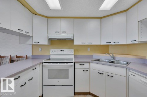 Kitchen featuring white cabinetry with black hardware, a stainless steel double sink, a white electric range, and integrated dishwasher - 316 2011 137 Avenue, Edmonton, AB - Indoor Photo Showing Kitchen With Double Sink