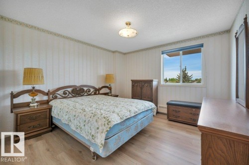 Bedroom featuring light wood-finish flooring, a window with exterior views, and striped wallpaper with a decorative border - 316 2011 137 Avenue, Edmonton, AB - Indoor Photo Showing Bedroom