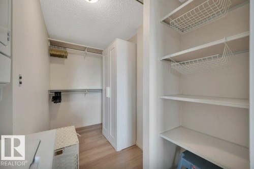 Laundry area featuring wood-finish flooring, overhead lighting, an integrated closet system with shelving and hanging rods, and an additional built-in shelving unit with wire baskets - 316 2011 137 Avenue, Edmonton, AB - Indoor With Storage
