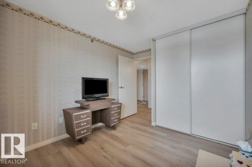 Bedroom featuring wood-finish flooring, patterned wallpaper with a decorative border, and a ceiling-mounted light fixture - 316 2011 137 Avenue, Edmonton, AB - Indoor