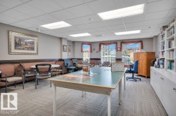Spacious common room featuring carpet tile flooring, extensive built-in shelving, large window fixtures, and ample natural light - 