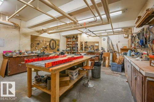 Spacious workshop featuring a large central workbench, exposed ceiling utilities, concrete flooring, extensive built-in cabinetry, and integrated task lighting - 316 2011 137 Avenue, Edmonton, AB - Indoor Photo Showing Garage