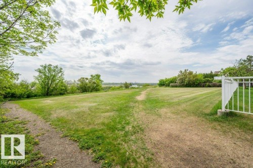 Expansive grassy area featuring a white picket fence, a winding dirt path, and mature trees bordering the property - 316 2011 137 Avenue, Edmonton, AB - Outdoor With View