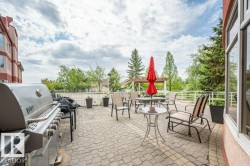 Expansive paver patio with a stainless steel outdoor grill, perimeter railing, and mature trees - 
