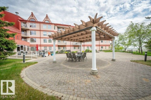 Paved patio featuring a large pergola, surrounded by mature greenery and a multi-story building with balconies - 316 2011 137 Avenue, Edmonton, AB - Outdoor