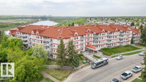 Multi-story residential building featuring a vibrant red roof, numerous balconies, and mature tree landscaping - 316 2011 137 Avenue, Edmonton, AB - Outdoor With Balcony With View
