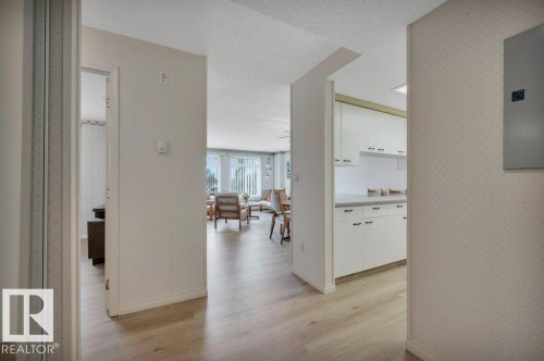 Light wood-finish flooring extending into the living area, white kitchen cabinetry with dark hardware, a dining area, and a bright living space with large windows - 316 2011 137 Avenue, Edmonton, AB - Indoor Photo Showing Other Room