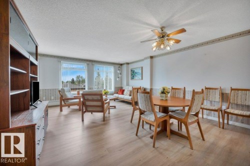 Open-concept living area featuring light wood-finish flooring, multiple windows with vertical blinds, a ceiling fan with integrated lighting, and a built-in wood shelving unit - 316 2011 137 Avenue, Edmonton, AB - Indoor Photo Showing Dining Room