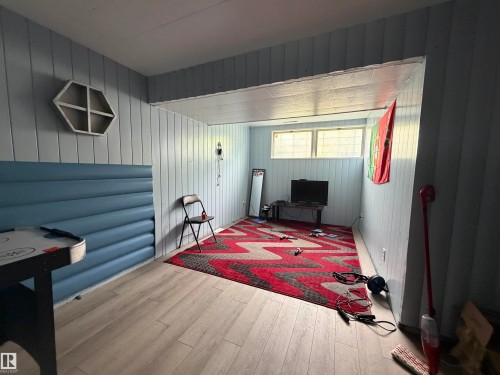 Room featuring wood-finish flooring, light blue vertical paneling, and a light blue padded wall accent - 5303 119 Avenue, Edmonton, AB 