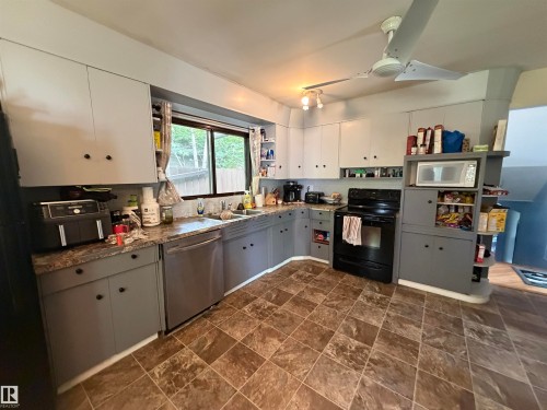 Kitchen featuring a built-in stainless-steel dishwasher, a black range with an overhead microwave, and a double-basin sink - 5303 119 Avenue, Edmonton, AB 