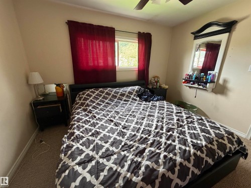 Carpeted bedroom featuring a ceiling fan, a window with red drapes, and a wall-mounted mirror - 5303 119 Avenue, Edmonton, AB 