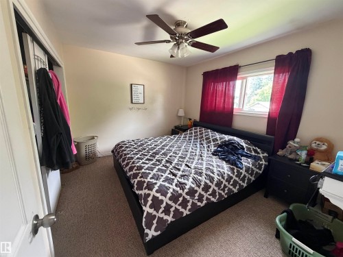 Bedroom featuring neutral wall paint, carpet flooring, a window with exterior visibility, a ceiling fan with light fixture, and a built-in closet with bifold doors - 5303 119 Avenue, Edmonton, AB 