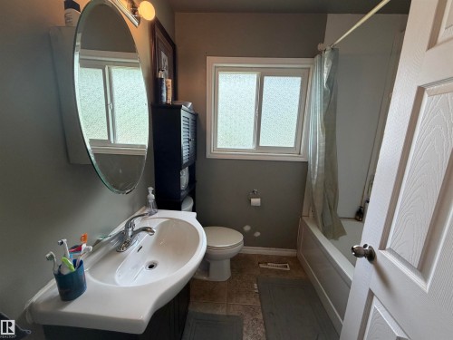 Bathroom featuring a ceramic pedestal sink with a chrome faucet, oval wall mirror, and built-in lighting - 5303 119 Avenue, Edmonton, AB 