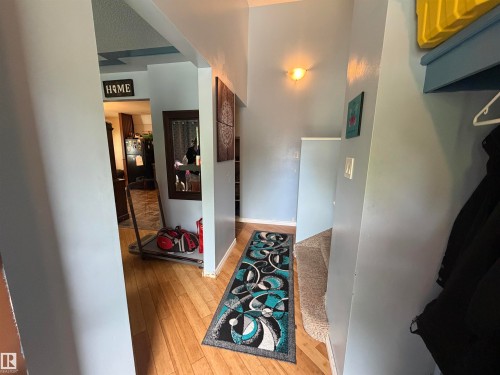 Hallway featuring wood-finish flooring, a wall-mounted light fixture, and an archway leading to an additional room - 5303 119 Avenue, Edmonton, AB 