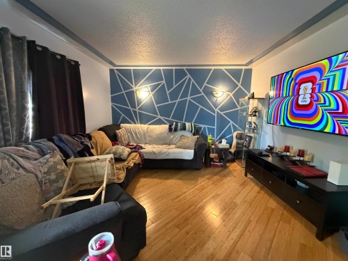Living area featuring wood-finish flooring, a decorative accent wall with geometric patterning, and wall-mounted sconces - 5303 119 Avenue, Edmonton, AB 