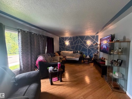 Living area featuring wood-finish flooring, a textured ceiling, and a distinct accent wall with geometric design and wall sconces - 5303 119 Avenue, Edmonton, AB 