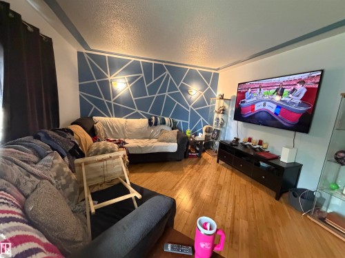 Living space featuring wood-finish flooring, a decorative accent wall, built-in wall sconces, and crown molding - 5303 119 Avenue, Edmonton, AB 