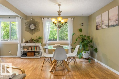 Bright dining area featuring wood-finish flooring, multiple windows, a chandelier-style light fixture, and neutral-toned walls - 171 Ridgewood, St. Albert, AB 