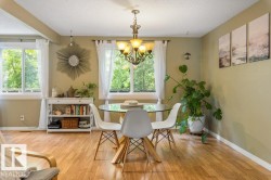 Bright dining area featuring wood-finish flooring, multiple windows, a chandelier-style light fixture, and neutral-toned walls - 