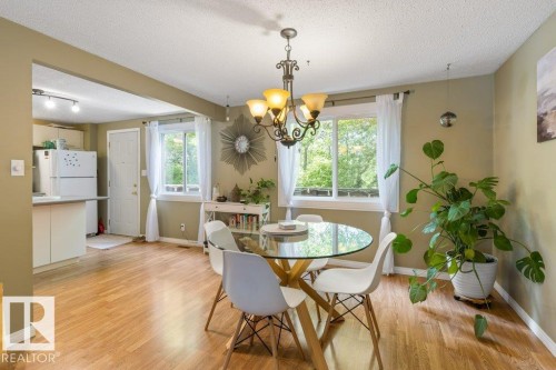 Open-concept living space featuring wood-finish flooring, a kitchen with white cabinetry, a built-in breakfast bar, and multiple windows - 171 Ridgewood, St. Albert, AB 