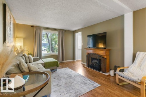Living space featuring a prominent fireplace with a wood mantel, wood-finish flooring, and a large window - 171 Ridgewood, St. Albert, AB 