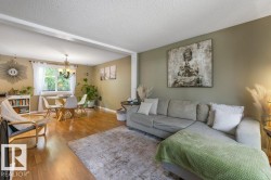 Open-concept living area featuring wood-finish flooring, a dining area with a chandelier, and a large window with natural light - 