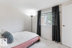 Carpeted room featuring a window with blinds and sheer black curtains, light-colored walls, a ceiling light fixture, and a white door with a brass-toned knob - 