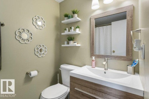 Bathroom featuring a wood-finish vanity with an integrated white sink, brushed nickel faucet, framed mirror, and floating wall shelves - 171 Ridgewood, St. Albert, AB 
