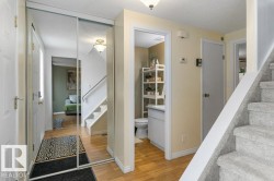 Entryway featuring wood-finish flooring, a full-length mirrored closet, and a carpeted staircase - 