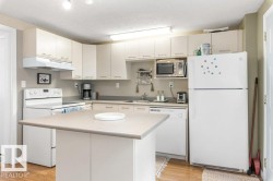 Kitchen featuring a central island with a solid surface countertop, white cabinetry with silver-tone hardware, wood-finish flooring, and white appliances including a range, refrigerator, and dishwasher - 
