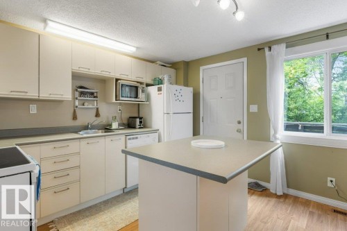 Kitchen featuring light wood-finish flooring, white cabinetry, a built-in dishwasher, and a center island with a light-toned countertop - 171 Ridgewood, St. Albert, AB 