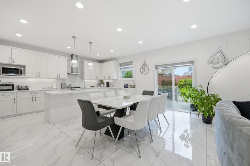 Open-concept kitchen and dining area featuring white shaker cabinetry, an expansive center island, pendant lighting, stainless steel appliances, and large format marble-look tile flooring - 76 Jacobs Close, St. Albert, AB 