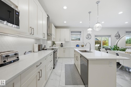 Open-concept kitchen featuring white cabinetry, light countertops, a hexagonal tile backsplash, and stainless steel appliances - 76 Jacobs Close, St. Albert, AB 