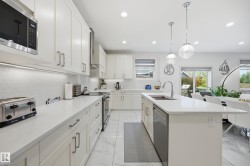 Open-concept kitchen featuring white cabinetry, light countertops, a hexagonal tile backsplash, and stainless steel appliances - 